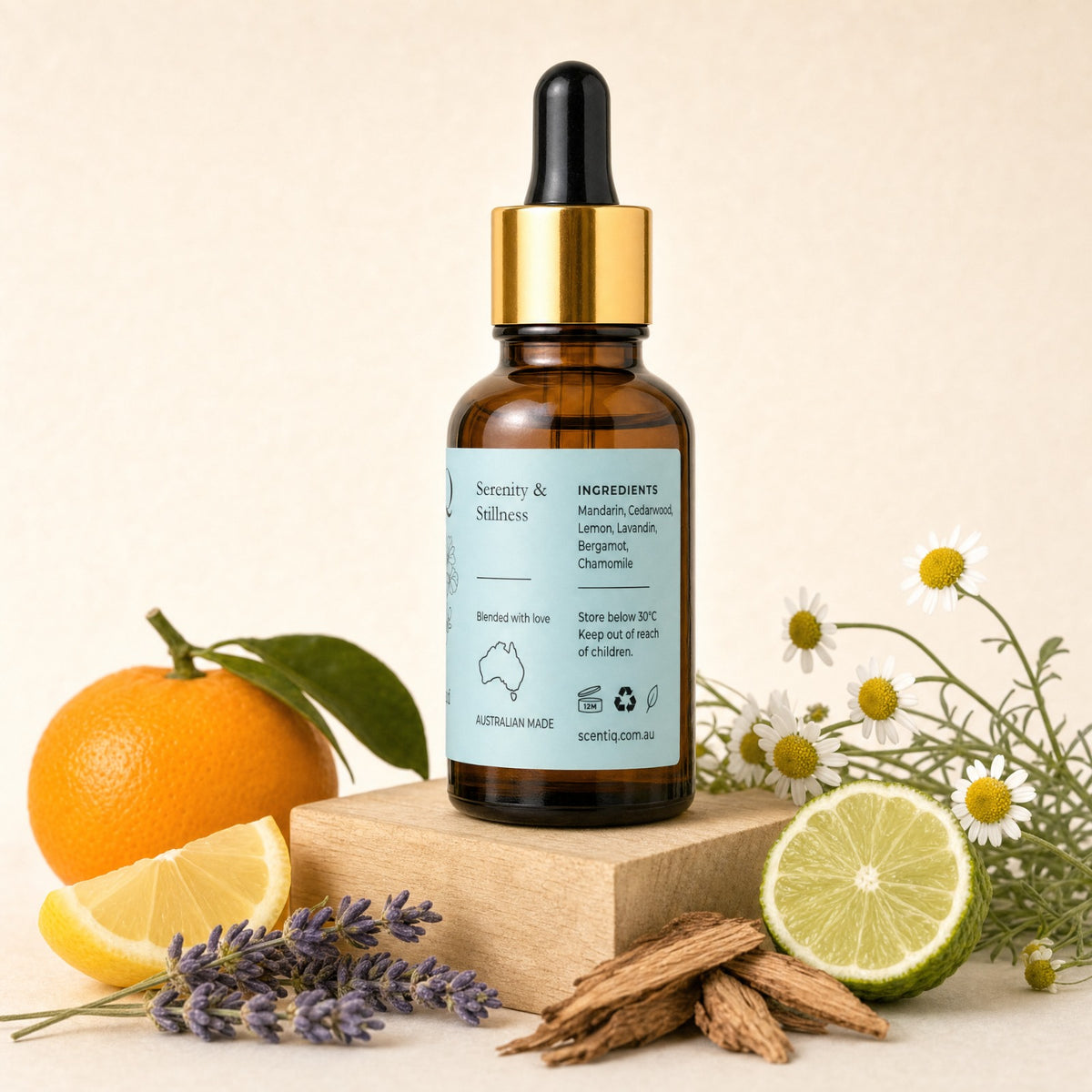 An amber glass dropper bottle with a gold collar and a pale blue label reading 'Sensuality & Selfcare' and 'Ingredients: Lemon, lavender, chamomile' stands on a wooden block. The bottle is styled with an orange, lemon slice, chamomile flowers, lavender sprigs, and cinnamon sticks on a warm beige background.