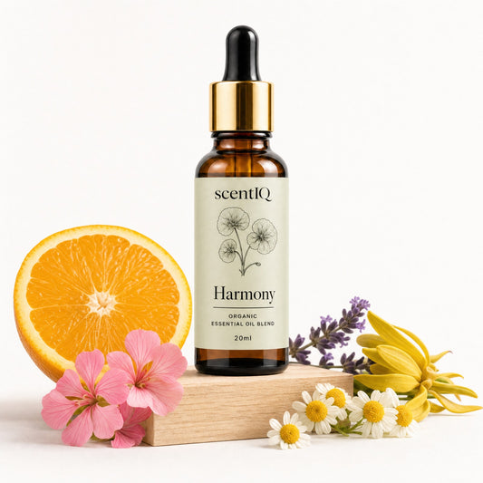 A 20ml amber glass dropper bottle of scentIQ Harmony Organic Essential Oil Blend, styled on a wooden block with a sliced orange, pink flowers, daisies, and lavender on a white background.