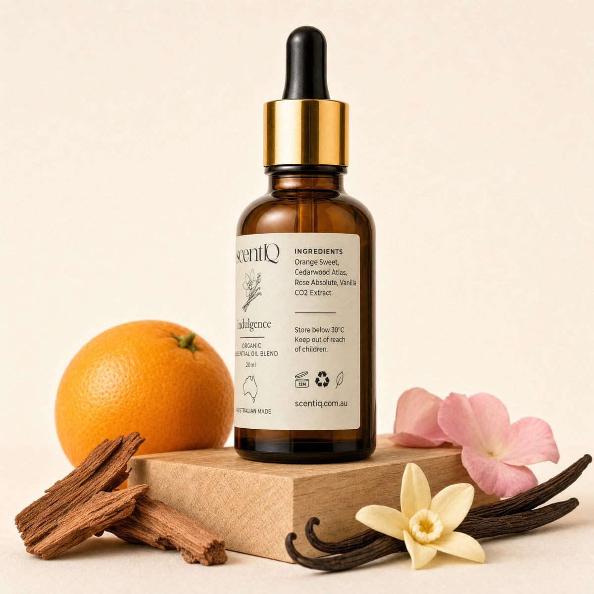 An amber glass dropper bottle labeled 'scentio' with a black rubber bulb and shiny gold collar, styled on a beige background with an orange, cinnamon sticks, vanilla beans, and pink flowers.